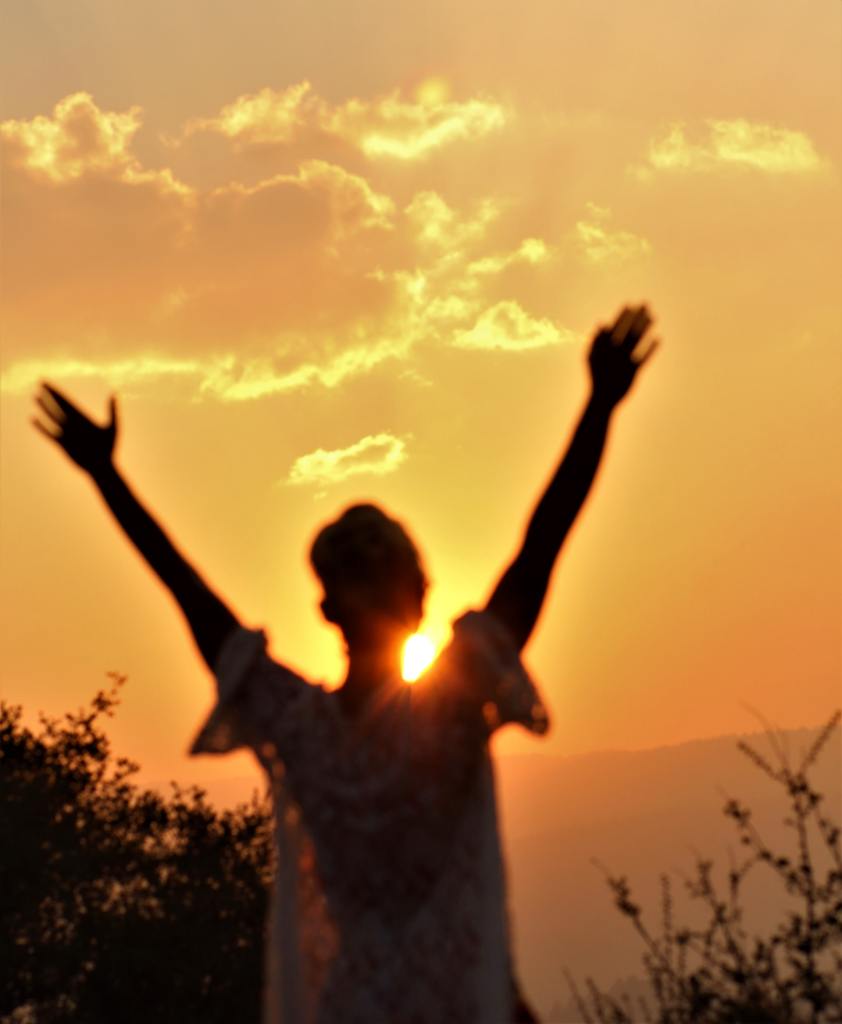 Žena okrenuta prema sunca s podignutim rukama